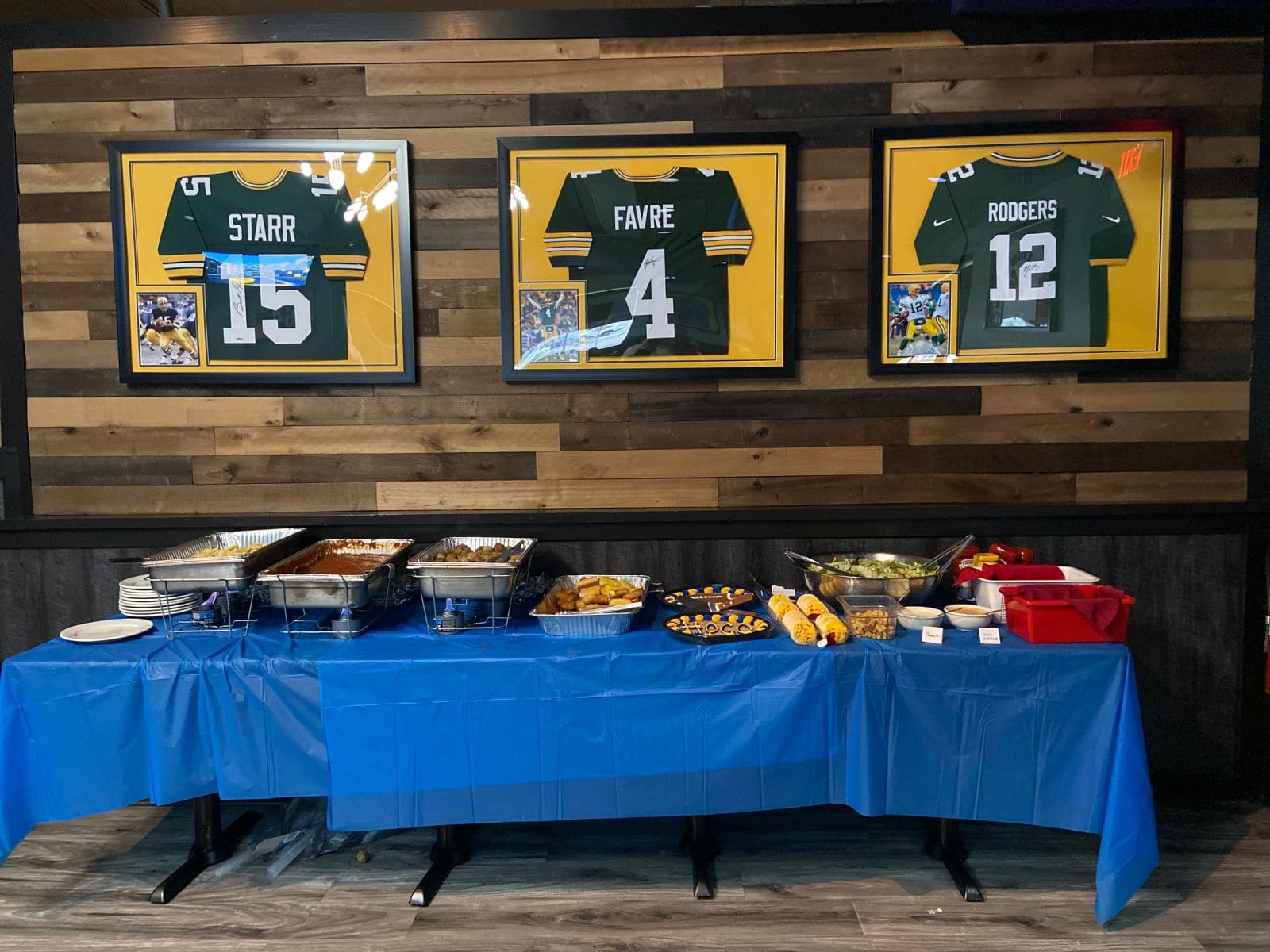A game-day buffet spread beneath framed Packers jerseys in the party room